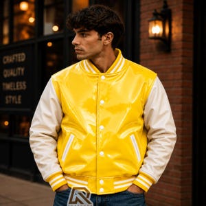 May include: A glossy yellow varsity jacket with white sleeves, a ribbed collar, cuffs, and hem featuring white stripes. The jacket has a front button closure with white buttons and two slanted side pockets with white trim, worn over blue jeans.