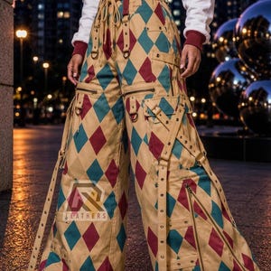 May include: Wide-leg trousers featuring a tan, teal, and maroon diamond harlequin pattern. The trousers include multiple adjustable straps with metal buckles, D-rings, and diagonal zippered pockets. A logo with the text AR LEATHERS is visible.
