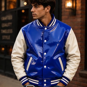 May include: A glossy royal blue varsity jacket with cream-coloured sleeves. The jacket features a ribbed collar, cuffs, and hem with white stripes, a snap-button front closure, and two side pockets with cream trim. A logo with the text R Leathers is visible.