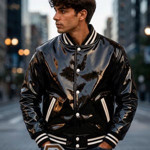 May include: A glossy black varsity jacket with a shiny patent finish, featuring a ribbed collar, cuffs, and hem with white stripes. The jacket has white snap buttons down the front and two side pockets with white trim. A logo with the text R LEATHERS.