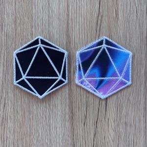 May include: Two embroidered patches in the shape of a 20-sided die. One is black with white stitching, the other features a blue and purple nebula design with white stitching. Both have a white border.