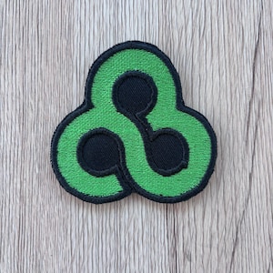 May include: A circular embroidered patch featuring a bright green triquetra-inspired knot design set against a solid black background. The patch has a thick, black stitched border that outlines the three interconnected loops of the green shape.