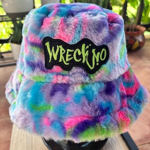 May include: A colorful bucket hat with a tie-dye pattern in shades of blue, purple, pink, and green. The hat features a black patch with the neon green text "WRECK'NO". The hat is made of a soft, fuzzy material.