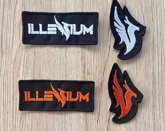 Peut inclure: Quatre écussons brodés. Deux écussons rectangulaires avec le mot "ILLENIUM" en blanc et orange, et deux écussons avec un motif d'oiseau stylisé en blanc et orange. Tous les écussons sont sur fond noir.