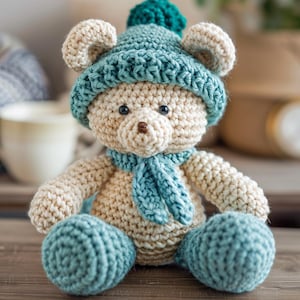 Peut inclure: Un ours en peluche au crochet fait à la main, de couleur crème et sarcelle. L'ours porte un chapeau sarcelle avec un pompon et une écharpe assortie. Les pattes et les pieds de l'ours sont sarcelle.