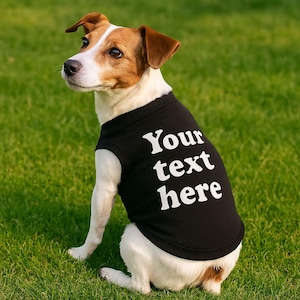 May include: A white and brown dog wearing a black sleeveless shirt with the text "Your text here" printed in white.