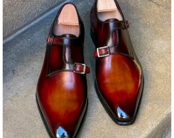 May include: A pair of polished, burgundy leather dress shoes with a double monk strap design. The shoes have a pointed toe and a rich, two-tone color gradient, transitioning from a deep burgundy to a lighter brown.
