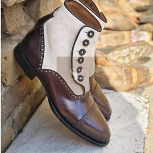 Puede incluir: Botas de tobillo de cuero marrón con una parte superior de ante blanco y cierre de botón. Las botas tienen un diseño de brogue y una punta puntiaguda.