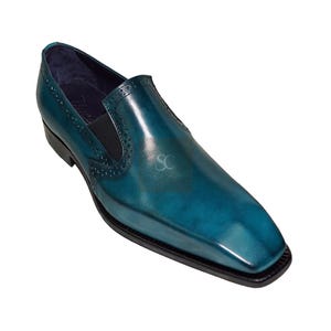May include: A single teal leather loafer with a square toe. The shoe has a glossy finish and a black sole. Decorative perforations are visible near the opening. The shoe is designed for formal or semi-formal occasions.