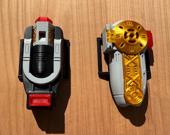 May include: Two futuristic-looking devices with a mix of colors. One is primarily black, gray, and red, while the other is gray and gold. Both have intricate designs and appear to be made of plastic.