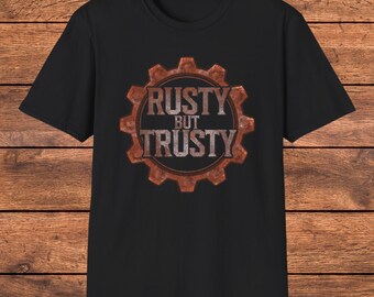 May include: A black short-sleeved t-shirt featuring a central graphic of a brown, textured gear. Inside the gear, the text RUSTY BUT TRUSTY is printed in a distressed, metallic-looking font with a weathered, oxidised appearance.