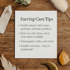 May include: A square white card with black text titled Earring Care Tips. The text lists instructions to avoid water, perfume, and hair products, store in a dry place away from sunlight, clean with a soft cloth, and handle with care.