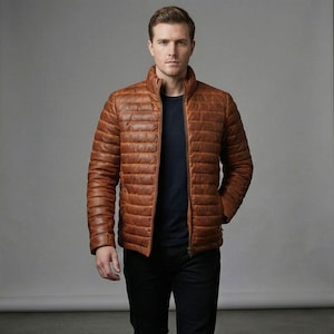 May include: A brown leather puffer jacket with a stand-up collar and a zipper closure. The jacket has horizontal stitching and a quilted design. The person in the image is wearing a navy blue shirt and black pants.