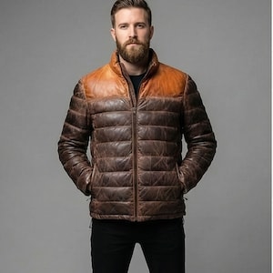 Könnte beinhalten: Braune Lederjacke mit Steppdesign. Die Jacke hat einen kontrastierenden, hellbraunen Lederbesatz auf den Schultern und einen durchgehenden Reißverschluss. Getragen über einem schwarzen Hemd.