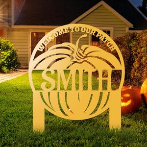 May include: A golden metal pumpkin-shaped garden sign with the family name "Smith" cut out. The sign reads "Welcome to our Patch" and is displayed in a front garden with lit jack-o'-lanterns.