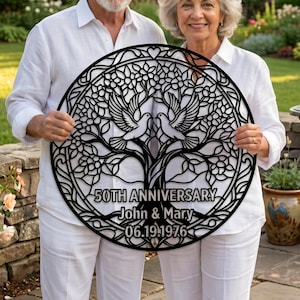 May include: A circular black metal wall art piece featuring an intricate tree of life design with two doves at the center. The text reads 50TH ANNIVERSARY, John & Mary, and 06.19.1976, all integrated into the decorative laser-cut metal frame.