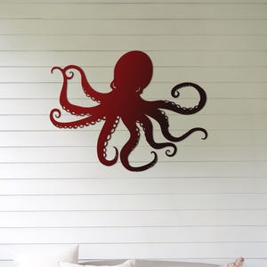 May include: A red metal octopus wall decor with a gradient of color from dark red to light red. The octopus is mounted on a white wall with white horizontal siding.
