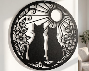 May include: A circular black metal wall art piece featuring a laser-cut design of two cats sitting side by side. The cats are surrounded by floral motifs and a sunburst pattern with a central circular sun, all enclosed within a solid black frame.