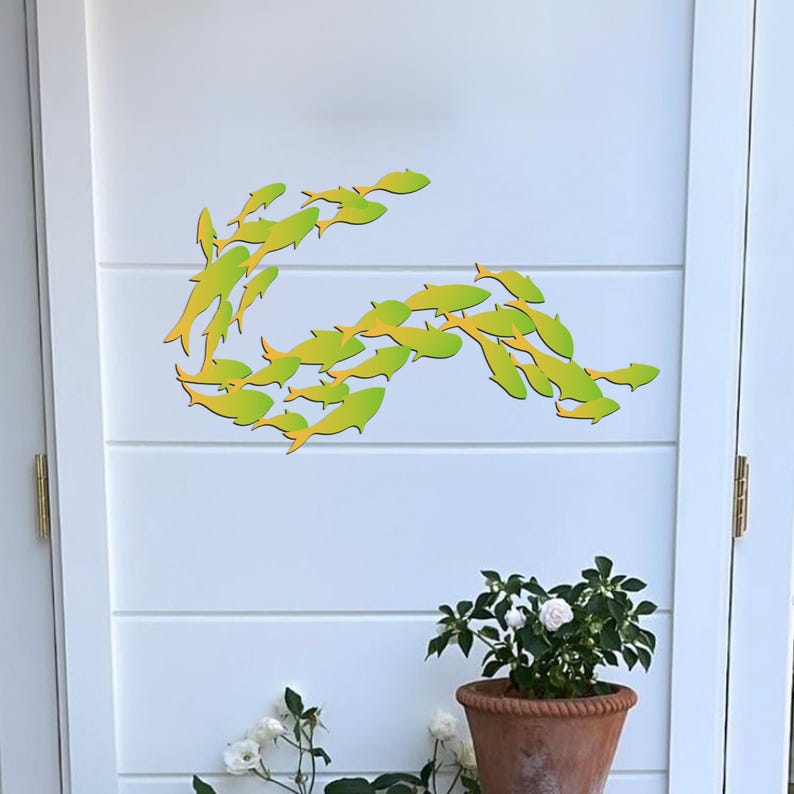 May include: A white door with a school of yellow and green fish cutouts on the surface. The fish are arranged in a curved shape, creating a wave-like pattern. There are two potted plants with white flowers in front of the door.