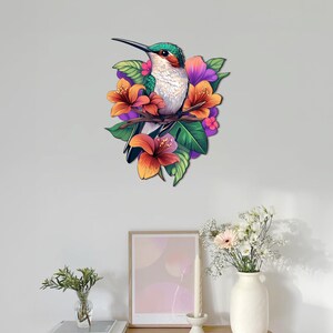 May include: A green and white hummingbird with a long beak perched on a branch with orange, purple, and green flowers.