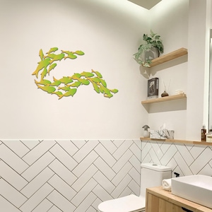 May include: A bathroom with white subway tile walls and a white toilet. A school of green and yellow fish are arranged in a curved shape on the wall above the toilet.