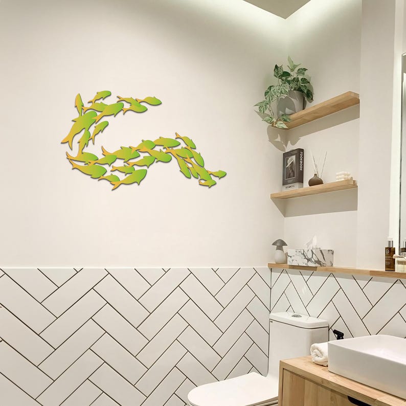 May include: A bathroom with white subway tile walls and a white toilet. A school of green and yellow fish are arranged in a curved shape on the wall above the toilet.