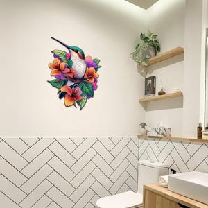 May include: A green and white hummingbird with a long beak perched on a branch with pink, orange, and purple flowers. The hummingbird is surrounded by green leaves. The image is a wall decor piece.
