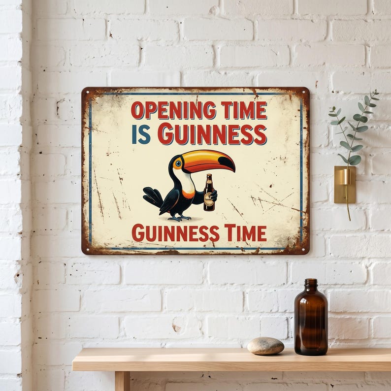 Op de afbeelding: Een rechthoekig metalen bord met een verweerde afwerking. Het bord toont een toekan die een fles Guinness vasthoudt. De tekst "OPENING TIME IS GUINNESS" en "GUINNESS TIME" is in het rood weergegeven. Het bord is bevestigd aan een witte bakstenen muur.