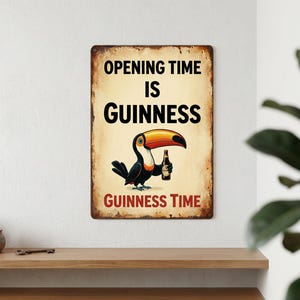May include: A vintage-style metal sign with a distressed finish. The sign features a cartoon toucan holding a bottle of Guinness. Text on the sign reads "OPENING TIME IS GUINNESS" and "GUINNESS TIME". The sign is mounted on a white wall.