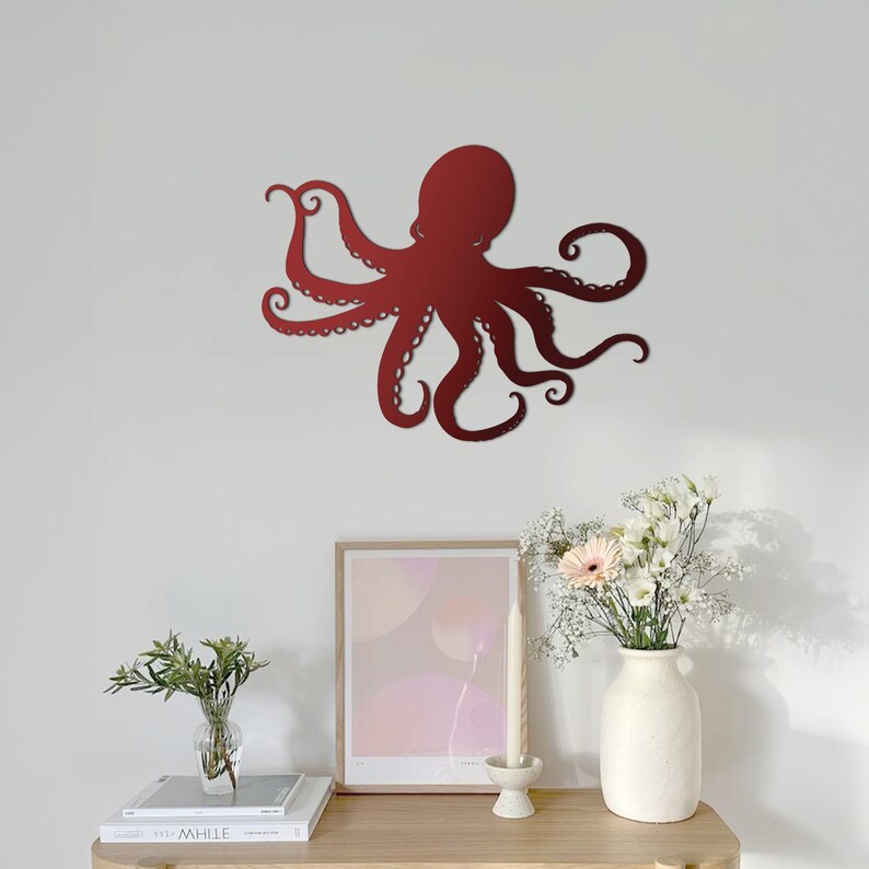 May include: A red metal octopus wall sculpture with a minimalist design. The octopus has eight tentacles and is mounted on a white wall.