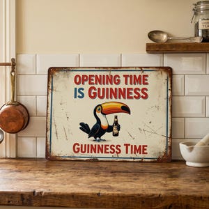 Op de afbeelding: Een metalen bord in vintage stijl met de tekst "OPENING TIME IS GUINNESS" in rood en blauw. Een toekan met een Guinness-fles staat in het midden. Het bord heeft een verweerde, verouderde uitstraling, geschikt voor een bar of keuken.