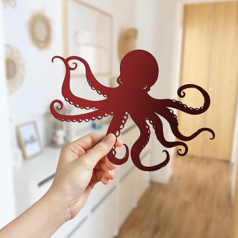 May include: A red paper cutout of an octopus with eight tentacles. The octopus is held in a person's hand.