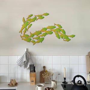 May include: A wall decor featuring a school of fish in a wave-like formation. The fish are made of wood and painted in shades of green and yellow.
