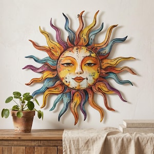 May include: A circular wall hanging featuring a stylised sun face with a distressed, multi-coloured finish. The sun has a central face with closed eyes and a serene expression, surrounded by radiating, wavy metal rays in shades of yellow, orange, blue, and purple.