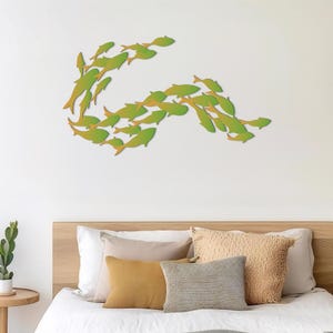May include: A white bed with a wooden headboard and a green fish wall decor. The bed is made with white bedding and has several throw pillows in beige and mustard yellow.