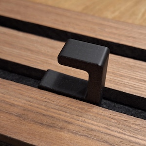 Pode incluir: Um gancho de metal preto montado em uma superfície de madeira com um forro de feltro preto.