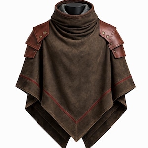 Puede incluir: Poncho marrón de ante con cuello alto y detalles de cuero en los hombros. El poncho tiene un diseño en capas con ribete rojo a lo largo de los bordes. Las piezas de cuero de los hombros están aseguradas con pequeños remaches redondos.