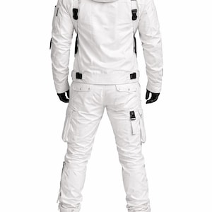 Pu&ograve; includere: Tuta da neve bianca con giacca con cappuccio e pantaloni abbinati. La giacca ha cinghie e fibbie nere, con tasche sulle maniche e sul petto. I pantaloni hanno tasche cargo e fibbie. L'outfit include stivali bianchi e guanti neri.