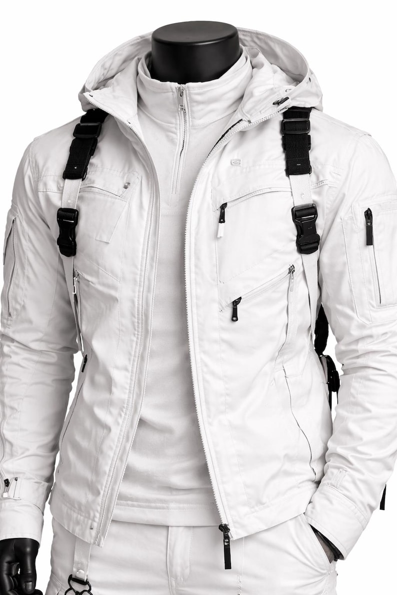 Pu&ograve; includere: Una giacca bianca con cappuccio, tasche multiple e cinghie nere con fibbie. La giacca ha una chiusura a zip ed &egrave; esposta su un manichino. La giacca fa parte di un completo bianco.