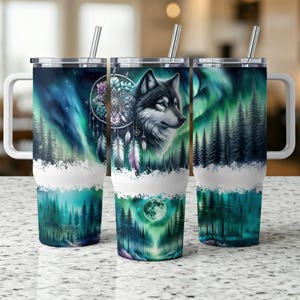 May include: Three stainless steel travel mugs with white handles and lids. Each mug features a different design: a wolf with a dreamcatcher, a forest scene with the Northern Lights, and a forest scene with a full moon. The mugs have a white band at the bottom.