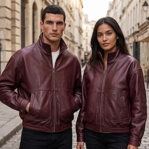 May include: Two matching burgundy leather jackets with high collars, full-length front zippers, and two large front pockets. The jackets feature long sleeves with ribbed cuffs and a ribbed hem, providing a structured fit with a smooth finish.