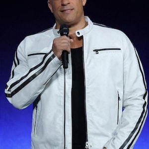 May include: A white leather jacket featuring a mandarin collar, a front zipper closure, and black vertical stripes running down the sleeves. The jacket is worn over a plain black shirt and is paired with matching white pants, while holding a microphone.