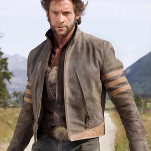 May include: A brown leather jacket featuring a high collar, a front zipper closure, and three horizontal tan stripes on each sleeve. The jacket is worn over a dark button-down shirt and blue jeans with a large, ornate metal belt buckle.