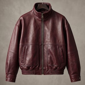 May include: A deep burgundy leather jacket featuring a high stand-up collar, a full-length front zipper, and two large front pockets with vertical openings. The jacket includes a ribbed hem and cuffs, with long sleeves and a smooth, polished finish.