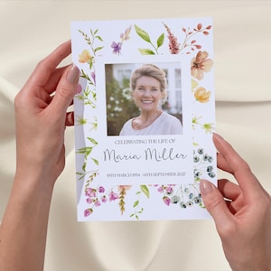 May include: A white memorial card with a watercolour floral border. A photo of a woman is in the centre of the card. The text "Celebrating the life of Maria Miller 19th March 1954 - 14th September 2022" is printed below the photo.
