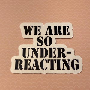 May include: A white sticker with the text "WE ARE SO UNDER-REACTING" in a bold, black font. The sticker is placed on a light pink background with a repeating wave pattern.