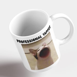 Puede incluir: Taza de cerámica blanca con una imagen en blanco y negro de un gato con la boca abierta, el texto "PROFESSIONAL YAPPER" está impreso en la taza.