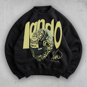May include: Black sweatshirt with the word "lando" in yellow block letters. A detailed graphic of a racing helmet is centered on the front. The helmet has a unique design with the Monster Energy logo and the driver's signature.