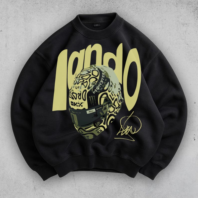 May include: Black sweatshirt with the word "lando" in yellow block letters. A detailed graphic of a racing helmet is centered on the front. The helmet has a unique design with the Monster Energy logo and the driver's signature.