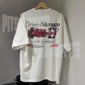 May include: White t-shirt with a red Formula 1 race car graphic and the text "The prince of Monaco" and "Circuit de Monaco".